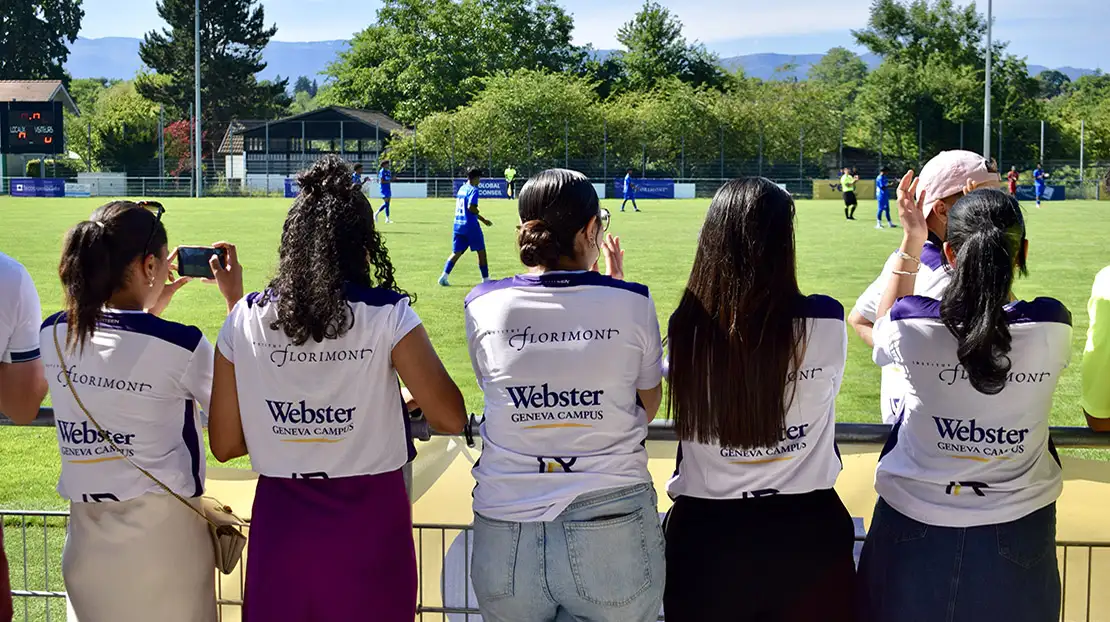 Four Students Facing the Field with Geneva Campus Written on Back of Their Shirts